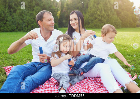 Glückliche Familie hat Spaß mit Seifenblasen auf dem Rasen im Park. Stockfoto