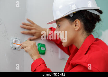 Weibliche Elektriker mit einem Schraubendreher an der Wand anbringen Stockfoto