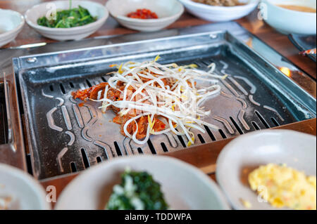 Gegrilltes mariniertes Schweinefleisch Kimchi mit bean Sprout gekrönt mit verschiedenen Beilagen Gemüse und Gewürze Saucen in einem koreanischen Restaurant gegessen Stockfoto