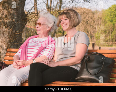 Gerne ältere Frau und Tochter sitzen im Park nach dem Einkaufen Stockfoto