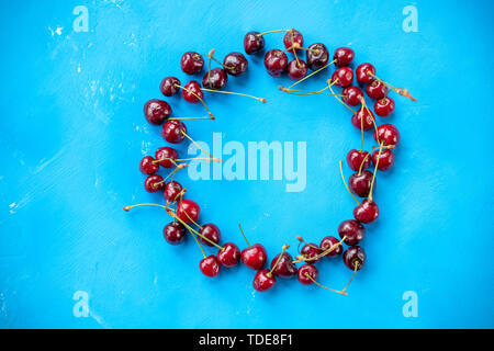 Köstliche reife rote Kirschen auf dem blauen Hintergrund im Kreis Rahmen angeordnet. kreatives Layout mit frischen reifen Beeren. cherry Hintergrund mit weißen Stockfoto