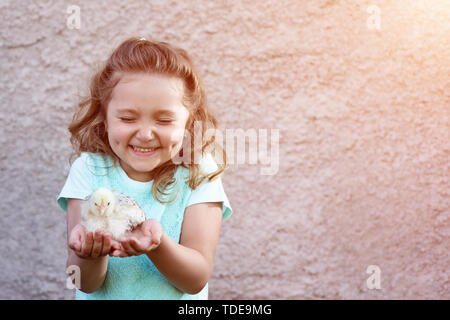 Ein nettes Mädchen in ein blaues T-Shirt mit Grübchen auf den Wangen hält ein Huhn in ihren Händen und Schiele mit Emotionen und Freude Stockfoto