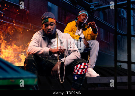 Zwei schwarze Rapper in Kappen sitzen am Feuer Stockfoto
