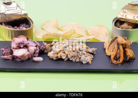 Sortiment von verschiedenen Arten von Meeresfrüchten in einem rustikalen schwarzen Stein Teller mit Pommes Frites und zwei Dosen, die das Foto auf einem grünen Tisch schmücken Stockfoto