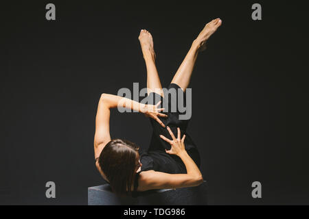 Soziale Thema. jungen kaukasischen Frau in seltsamen in Kleidung darstellen Posing auf Black Cube, dunklen Hintergrund, symbolisiert, die Schmerzen, Leiden, die Hilfe suchen, protecti Stockfoto