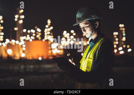 Asiatischer mann Ingenieur mit digitalen Tablet arbeiten bis spät in die Nacht schicht am Erdöl Raffinerie in Industrial Estate. Chemie-, Brennstoff- und Stromversorgung Stockfoto