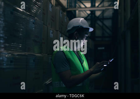 Seitenansicht des Asiatischen junge lagerarbeiter Mann mit Sicherheit hart hat ist überprüfen Sie den Details mit einem digitalen Tablet bei der Inventur Zimmer Stockfoto
