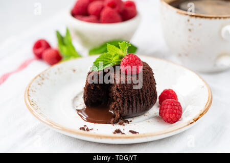 Warme Schokolade Lava Kuchen mit Bissen aus geschmolzenem Zentrum und Himbeeren auf Weiß Dessertteller genommen. Detailansicht Stockfoto
