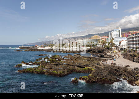 Lava Felsen und Klippen entlang der Küste im Zentrum von Puerto de la Cruz. Lagos Martianes im Hintergrund. Blauer Himmel und schöne Wolken über moun Stockfoto