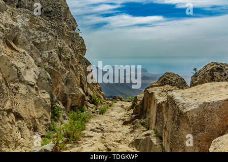 Steinigen weg im Hochland von Pinien am sonnigen Tag umgeben. Klar lue Sky und einige Wolken am Horizont. Rocky tracking Straße in trockenen Berg Stockfoto