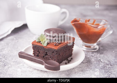 Ein Stück leckere hausgemachte Schokolade Kuchen auf den Teller mit Puderzucker, minzblatt und Schokolade Löffel auf grauem Hintergrund Stockfoto