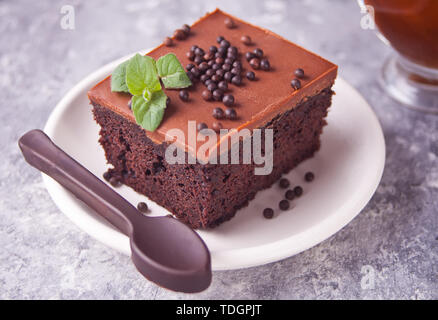 Ein Stück leckere hausgemachte Schokolade Kuchen auf den Teller mit Puderzucker, minzblatt und Schokolade Löffel auf grauem Hintergrund Stockfoto