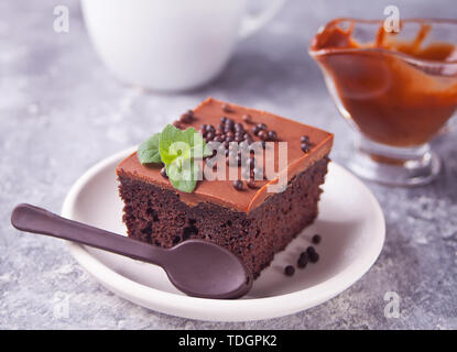 Ein Stück leckere hausgemachte Schokolade Kuchen auf den Teller mit Puderzucker, minzblatt und Schokolade Löffel auf grauem Hintergrund Stockfoto
