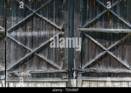 Eine große Tür in den Stall aus Holz. Alte Platten drehte sich Grau. Elemente der alten ländlichen Gebäude. Stockfoto