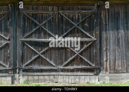 Eine große Tür in den Stall aus Holz. Alte Platten drehte sich Grau. Elemente der alten ländlichen Gebäude. Stockfoto