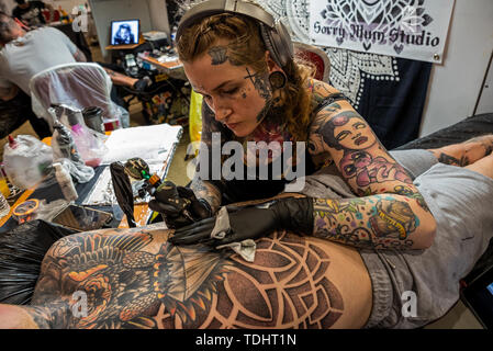 Milton Keynes, UK. Die britische Tattoo Fest fand am Marshall Arena über das Wochenende des 15. und 16. Juni 2019. Über 190 Arbeiten Tattoo Künstler waren anwesend, plus den Handel geht. Bild Laura dot Firth von der traurige Mamma Studio tätowieren Brust entspannte Menschen. Credit: Stephen Bell/Alamy. Stockfoto