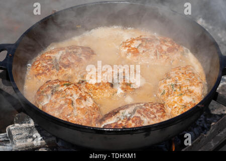 Köstliche Wild Rot Lachs Fisch Schnitzel mit Soße gebraten in heißen Bratpfanne braten auf Kohlen, über offenem Feuer am Lagerfeuer. Kochen auf Feuer während Picknick o Stockfoto