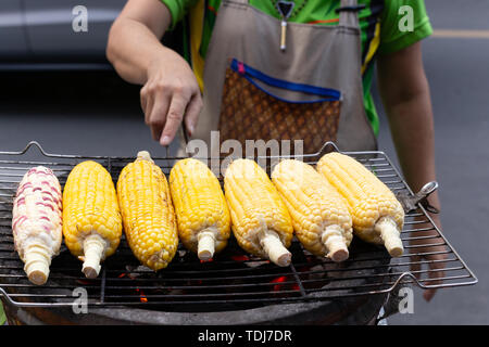 Street Food Frau Grill Maiskolben auf den heißen Herd mit Holzkohle. Stockfoto