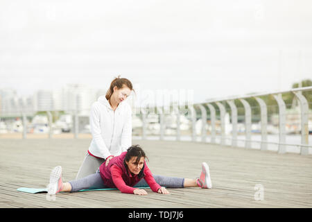 In voller Länge Porträt des zeitgenössischen reife Frauen Yoga im Freien mit weiblichen Kursleiter helfen, Platz kopieren Stockfoto