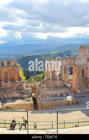 Taormina, Sizilien, Italien - Apr 8 2019: Tolle Aussicht von den antiken griechischen Theater von Taormina. Ruinen von historische Sehenswürdigkeit. Ätna Silhouette in den Wolken im Hintergrund. Beliebte touristische Ort. Stockfoto