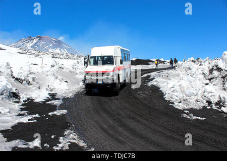 Ätna, Sizilien, Italien - Apr 9 2019: Touristische Jeep oder Bus fahren Touristen auf den Gipfel des Vulkan Ätna und zurück. Schnee auf dem vulkanischen Boden entlang der Straße. Ganz oben im Hintergrund. Stockfoto