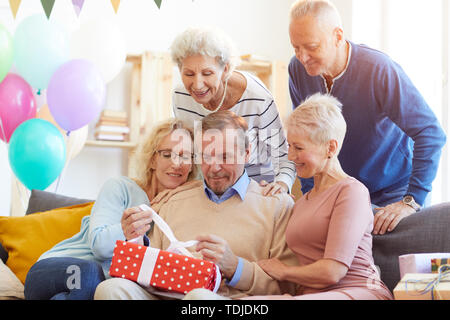 Inhalt gut aussehender bärtiger Mann in Pullover sitzen auf dem Sofa und öffnen Geburtstagsgeschenke unter Freunden zu Hause. Stockfoto