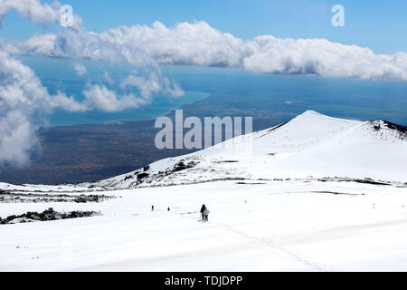 Herrliche Aussicht von den Ätna fotografiert mit Wanderern hinunter auf den Schnee und das Meer im Hintergrund. Herrliche Wolken in der Nähe der Gipfel des Berges. Ätna, Sizilien, Italien. Stockfoto