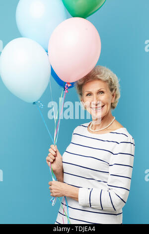 Portrait von verspielten hübsche reife Frau in abgestreift Pullover holding Haufen der bunten Ballone Stockfoto
