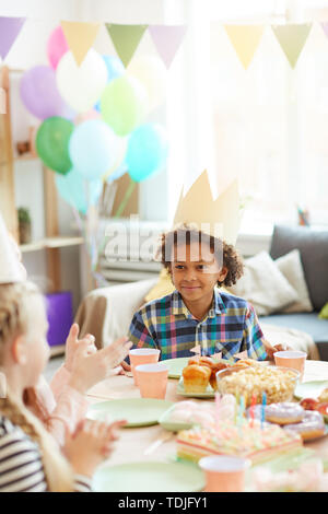 Portrait von lächelnden Afrikaner - Junge tragen Krone sitzen am Tisch beim Feiern Geburtstag mit Freunden Stockfoto