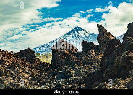 Berg Teide mit weißem Schnee Flecken, die teilweise durch die Wolken bedeckt. Strahlend blauen Himmel. Riesige Lavafelsen im Vordergrund. Nationalpark Teide, Teneriffa, Stockfoto