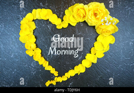 Guten Morgen Konzept mit Text in Herzen von frischen gelben Rosen und Blüten auf schwarzem Marmor Hintergrund. Stockfoto