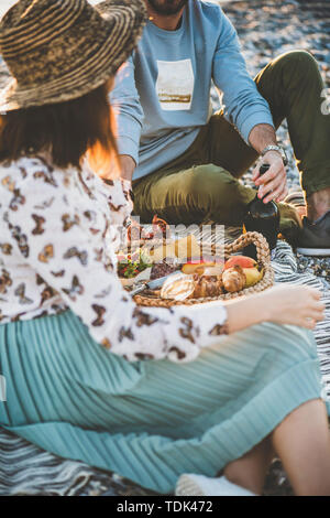 Sommer Picknick am Strand bei Sonnenuntergang. Junges Paar sitzt auf Decke in Wochenende Picknick im Freien am Meer mit frischem Obst, leckere Häppchen ein Stockfoto