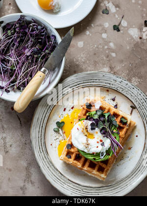 Waffel Frühstück mit pouched Ei auf Avocado überstieg Rose mit radieschen Sprossen in rustikale Platte serviert. Stockfoto