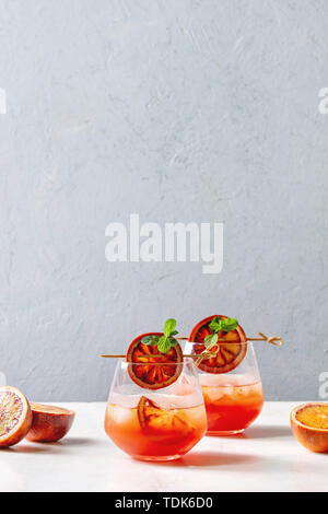Blutorange Eistee Cocktails in Gläser, durch die Scheibe der Orangen und frischer Minze auf spieße eingerichtet, auf weissem Marmor tisch mit grauen Wand diente an Backgr Stockfoto