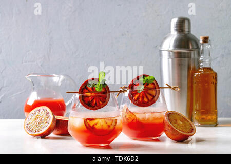 Blutorange Eistee Cocktails in Gläser, durch die Scheibe der Orangen und frischer Minze auf spieße eingerichtet, serviert mit Shaker, Kanne Saft, Flasche Rum auf wh Stockfoto