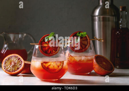 Blutorange Eistee Cocktails in Gläser, durch die Scheibe der Orangen und frischer Minze auf spieße eingerichtet, serviert mit Shaker, Kanne Saft, Flasche Rum auf wh Stockfoto