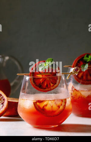 Blutorange Eistee Cocktails in Gläser, durch die Scheibe der Orangen und frischer Minze auf spieße eingerichtet, auf weissem Marmor tisch mit grauen Wand diente an Backgr Stockfoto