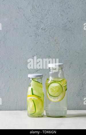Sommer Getränke Thema. Zwei Glasflaschen mit Zitrone und Gurke Infusion sassy Wasser auf weißem Marmor tisch mit Beton Wand im Hintergrund. Platz kopieren Stockfoto