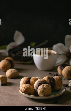 Baci di dama hausgemachte italienische Haselnuss Kekse Kekse mit Schokolade in Keramik Platte mit Tasse Espresso und Magnolia Blumen serviert. Stockfoto