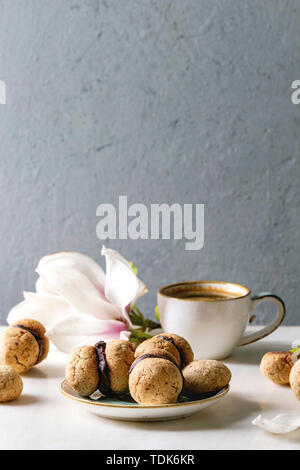 Baci di dama hausgemachte italienische Haselnuss Kekse Kekse mit Schokolade in Keramik Platte mit Tasse Espresso und Magnolia Blumen serviert. Stockfoto