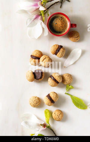 Baci di dama hausgemachte italienische Haselnuss Kekse Kekse mit Schokolade mit roten Tasse Espresso und Magnolia Blumen über weiß ma serviert. Stockfoto