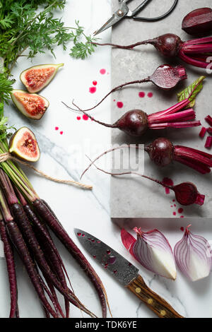 Baby, rote Beete, Karotten Lila, Lila Zwiebeln und Feigen, in Scheiben geschnitten, und auf einem Marmor Fliesen Oberfläche bereit. Ein Messer, Schere und einem Marmorbad board i Stockfoto