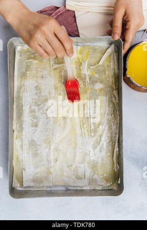 Frau Verbreitung zerlassener Butter auf Baklava griescreme Blätter mit einem Pinsel in ein Backblech Stockfoto