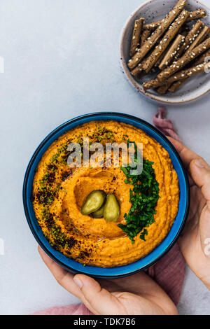 Frau geröstete Paprika hummus in blauer Schüssel garniert mit Petersilie, Pistazie, sumach und Dill Pickles von Cracker begleitet. Stockfoto