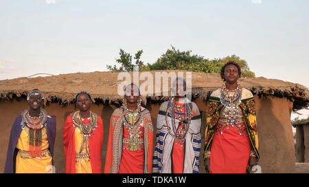 Weite Einstellung auf fünf Masai Frauen in traditioneller Kleidung singen und tanzen in einem Dorf in der Nähe der Masai Mara, Kenia Stockfoto
