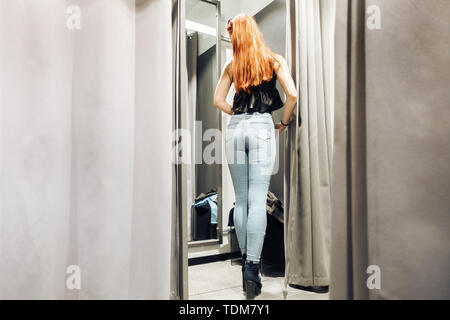 Junge schlanke Mädchen, das versuchte auf neuen Jeans im Proberaum im Store. Frau mit schönen Abbildung sieht sich selbst in der Reflexion der Spiegel. Pu Stockfoto