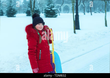 Portrait von kleinen Mädchen im Winter. das Kind in hat Lächeln ist und das Fell ist Holding sleigh Schläuche. schneit Stockfoto