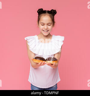 Fröhliches kleines Mädchen genießen Sie Schokolade donuts abgedeckt Stockfoto