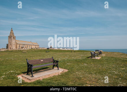 Vier Parkbänke mit Blick aufs Meer in Newbiggin durch das Meer in Northumberland mit St Bartholomews Church und die newbiggin Time Capsule Denkmal in Stockfoto