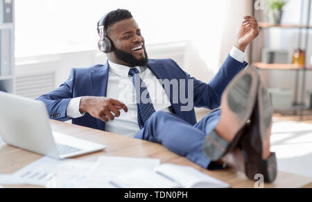 Junge afrikanische Arbeiter mit Beinen am Tisch spielen auf virtuellen Gitarre Stockfoto